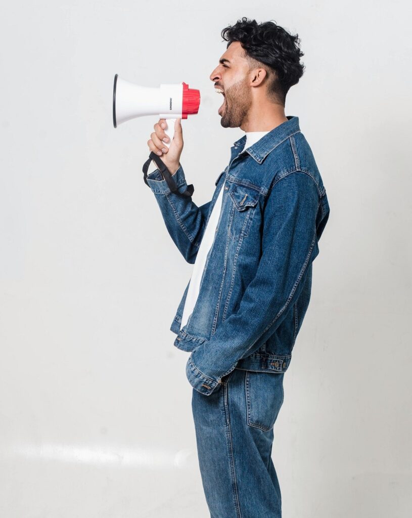 A black man shouting an announcement into a megaphone.