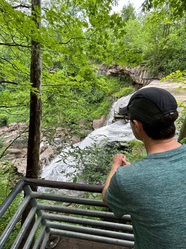 A man with a cap looks over a railing at Brandywine Falls.