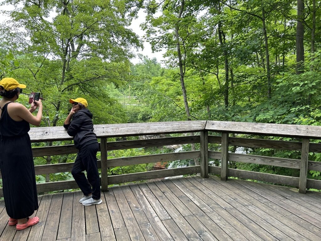 Two women take pictures over a railing near a waterfalls.