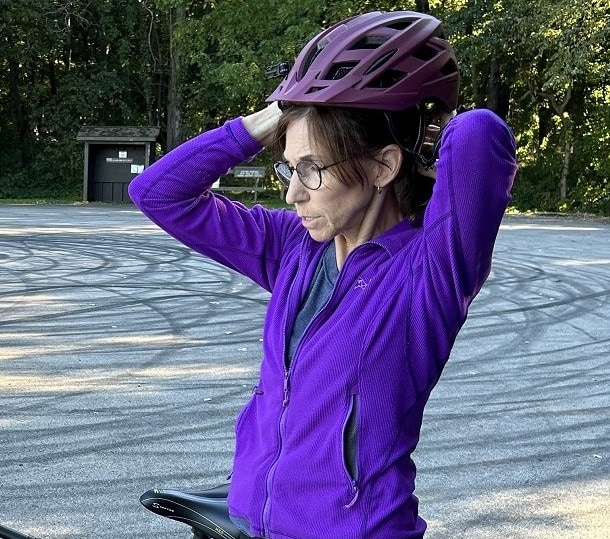 A woman in a purple sweatshirt puts her bike helmet on.