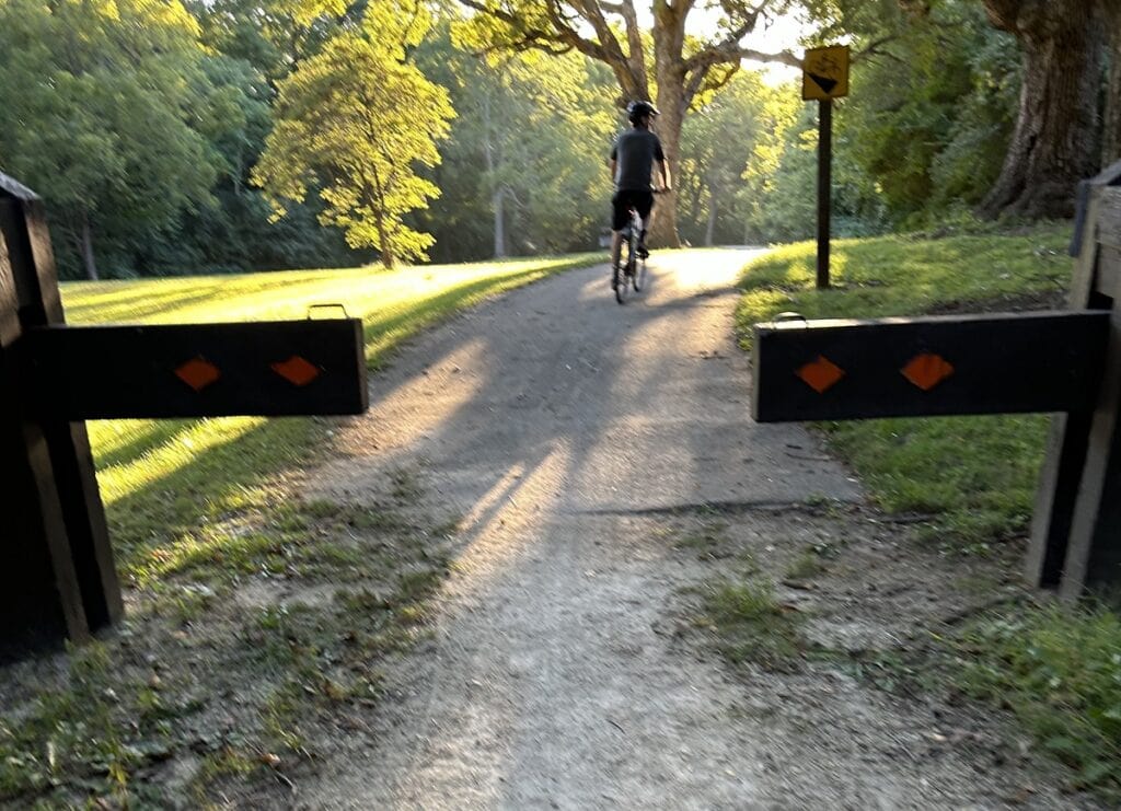 A man on a bicycle passes through a gate to a paved path.
