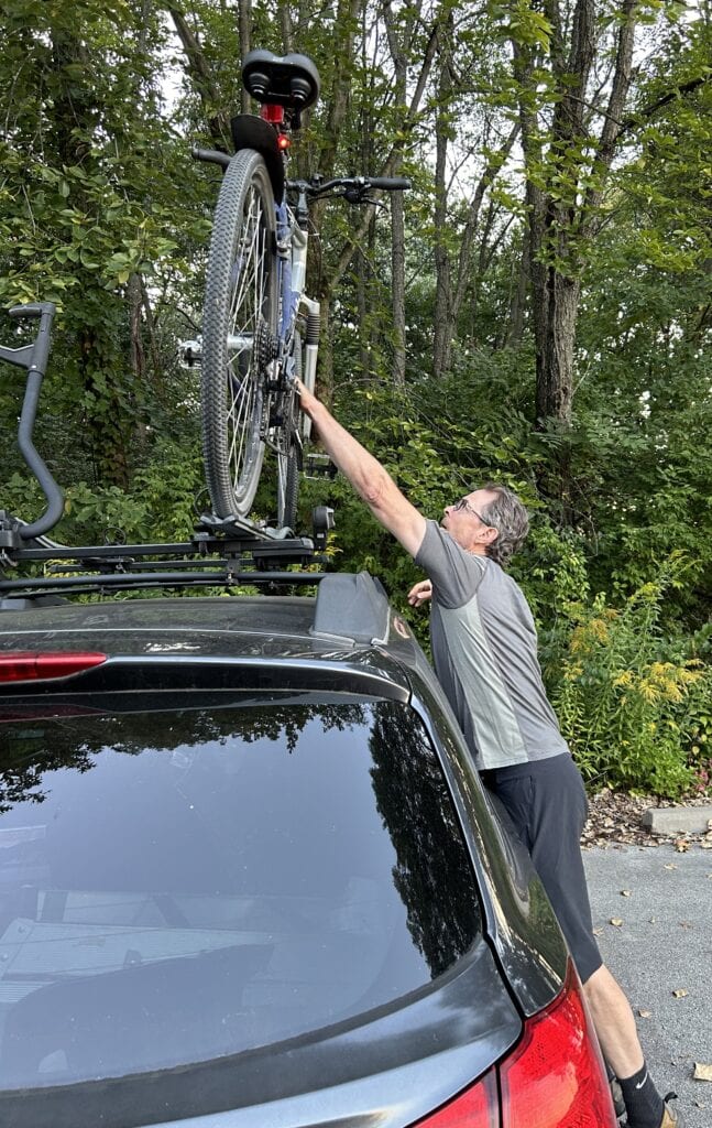 A man lifts a bike off from the top of a car.