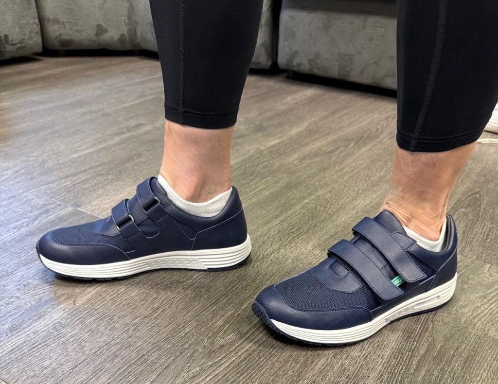 Two blue shoes with Velcro straps are shown by wearer.