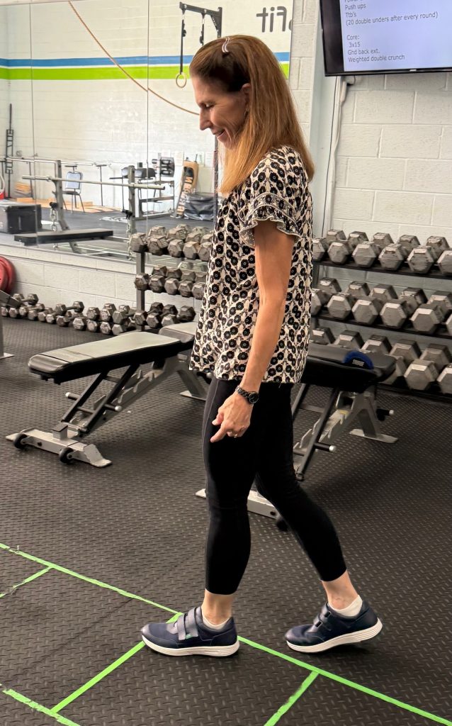 A woman smiles as she walks slowly with blue shoes on as if she's testing them.