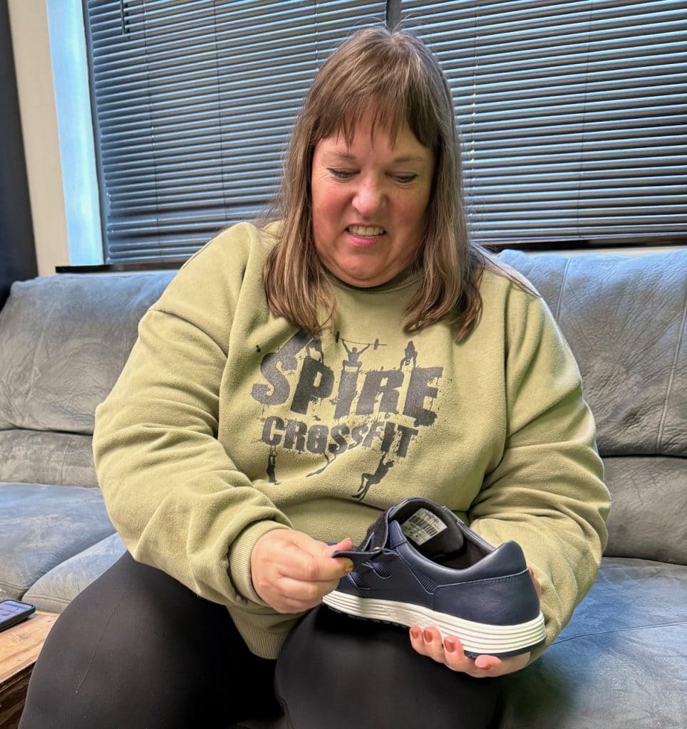 A woman in a sweatshirt holds a blue shoe and prepares to pull the Velcro strap