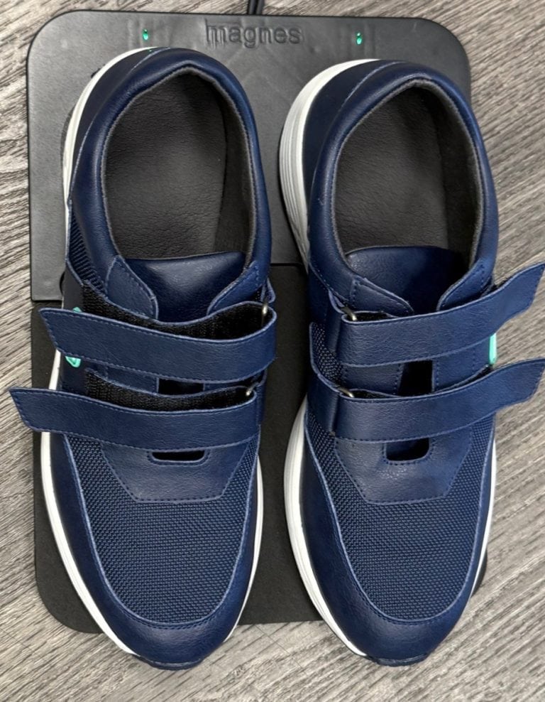 A pair of blue shoes with Velcro straps sits on a charger pad.