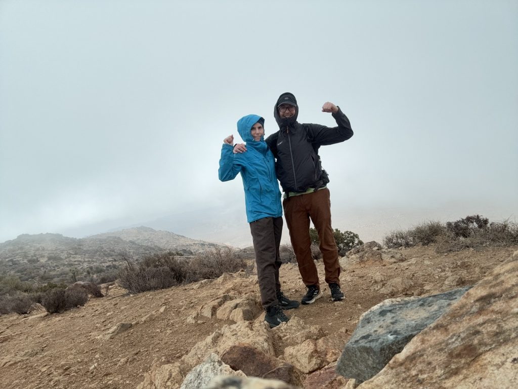 A man and woman hiker stand side by side at the top of a mountain.