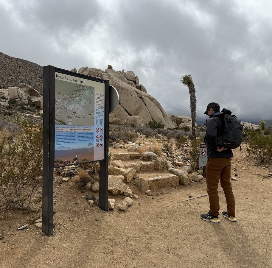 A male hiker reads the sign at a trailhead on a desert route.