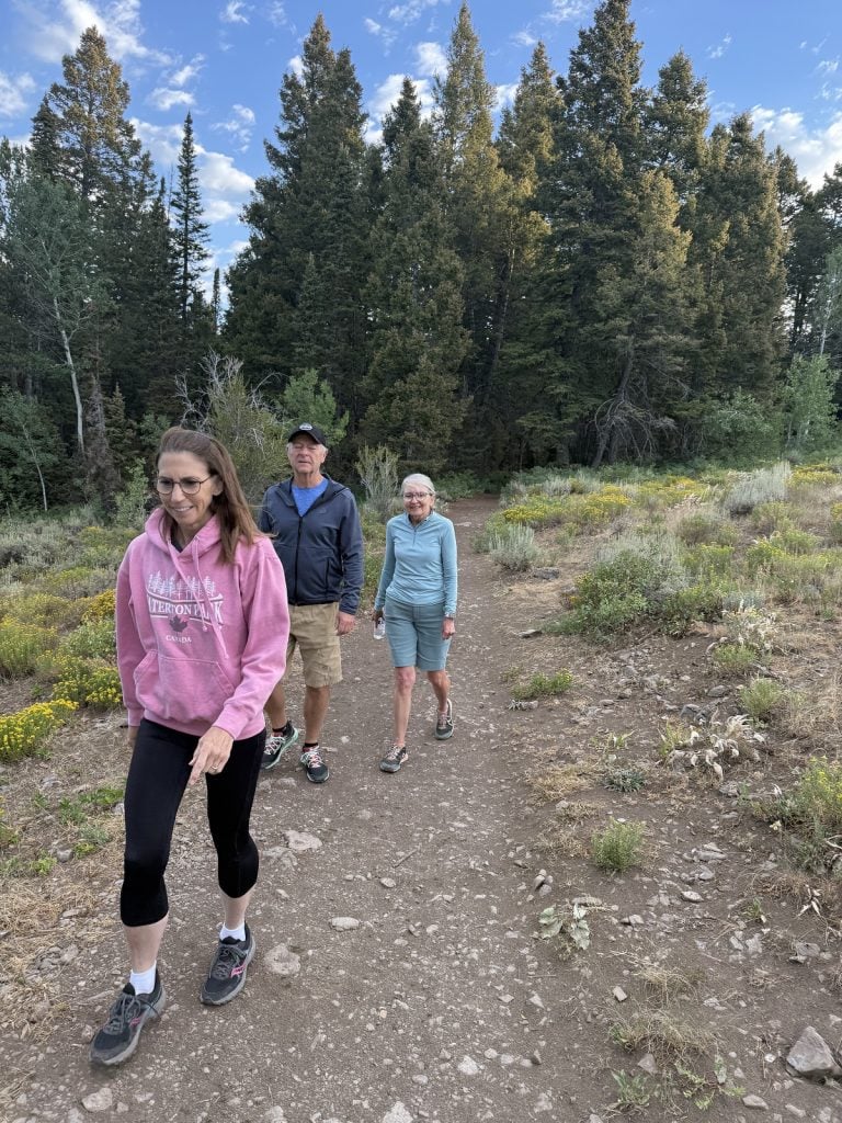 Three people including two women and one man hike a trail.