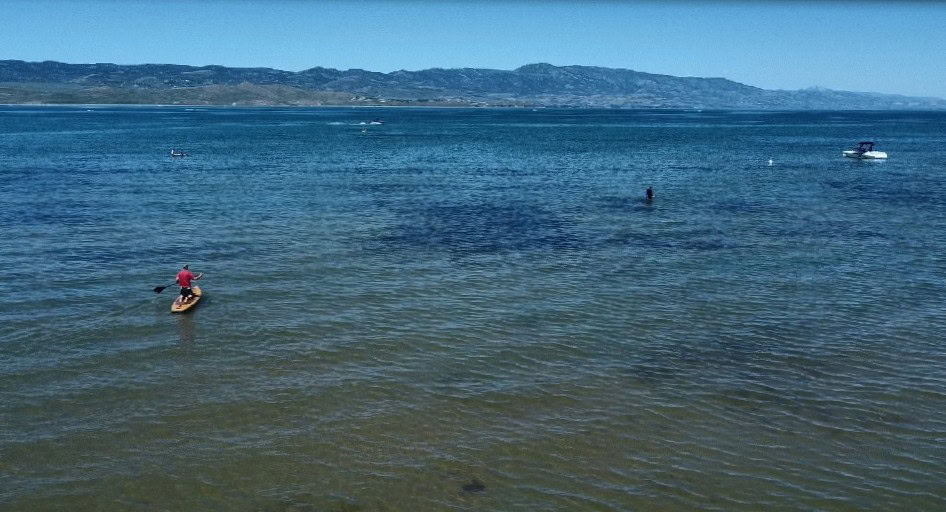 A deep blue lake has paddleboarders and boaters on it.