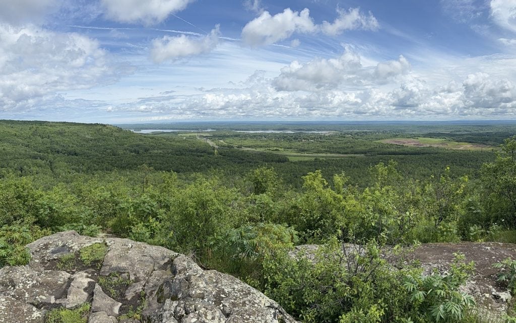A view from a peak shows a river and a cloudy and blue sky.