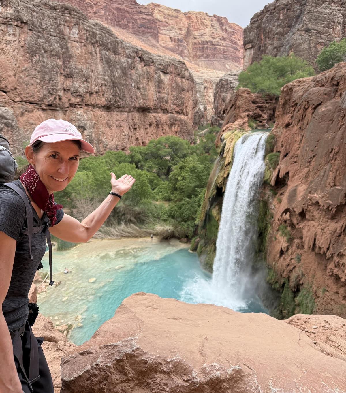 A woman points to a waterfall behind her.