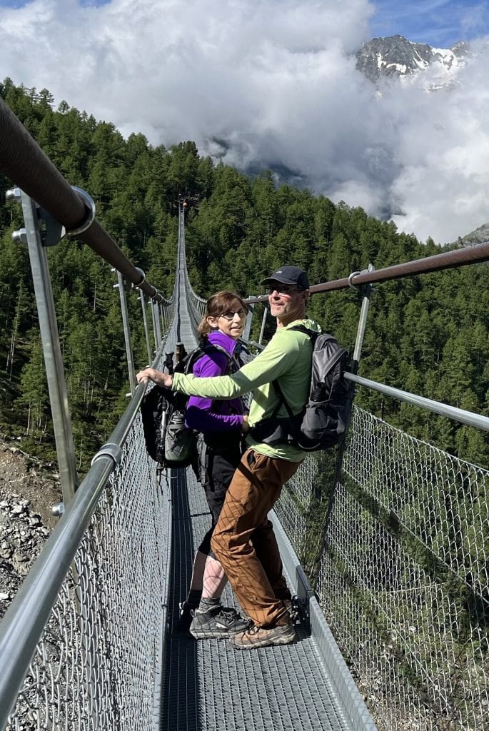 A man and woman lean up against the sides of a suspension bridge.
