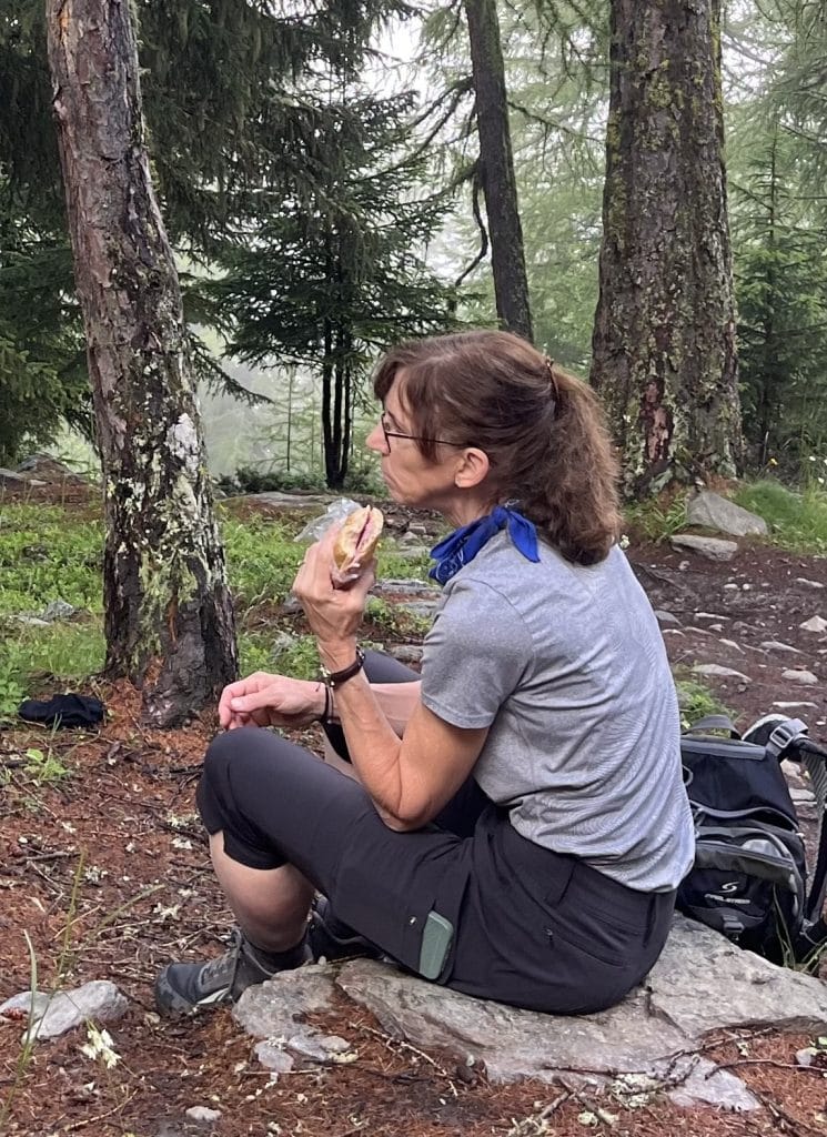 A woman sits on a rock eating a sandwich.