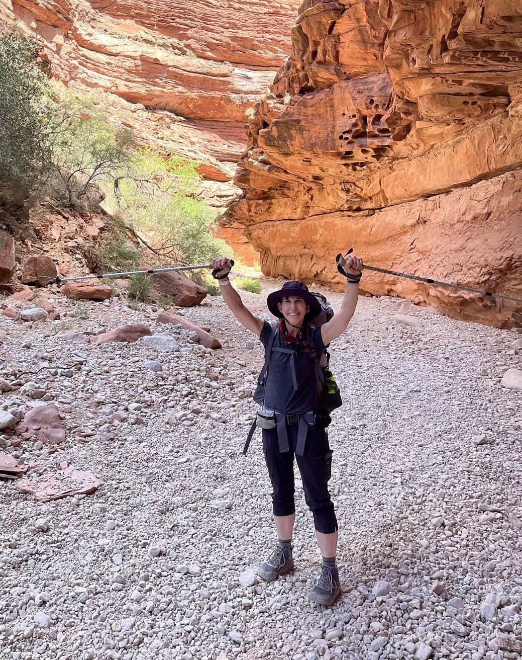 A woman holds up her poles on a hiking trail.