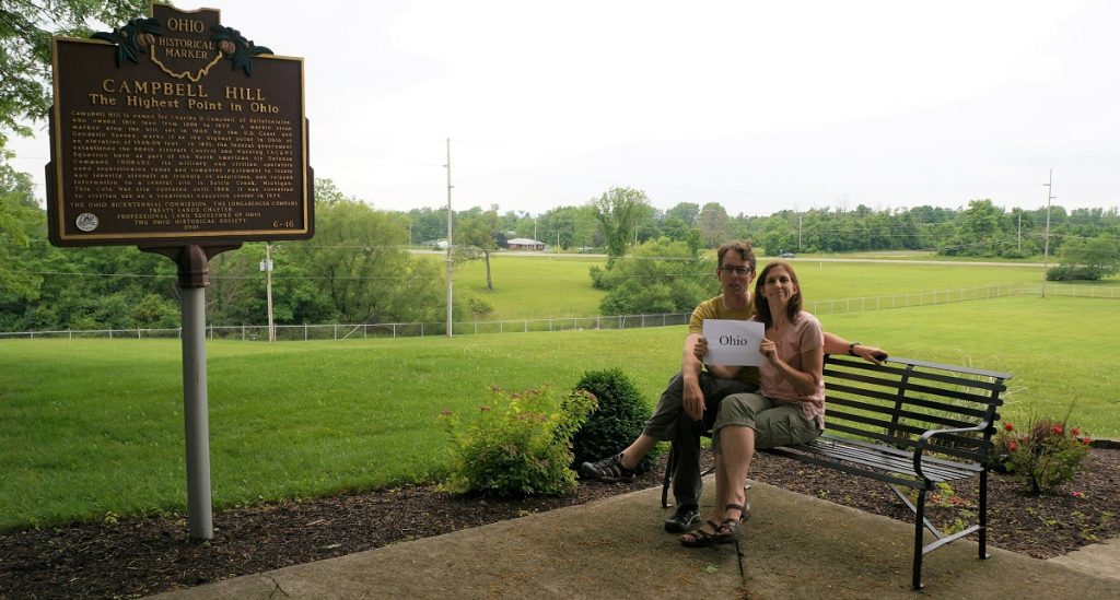 A man and woman sit on a bench holding a sign that says Ohio.