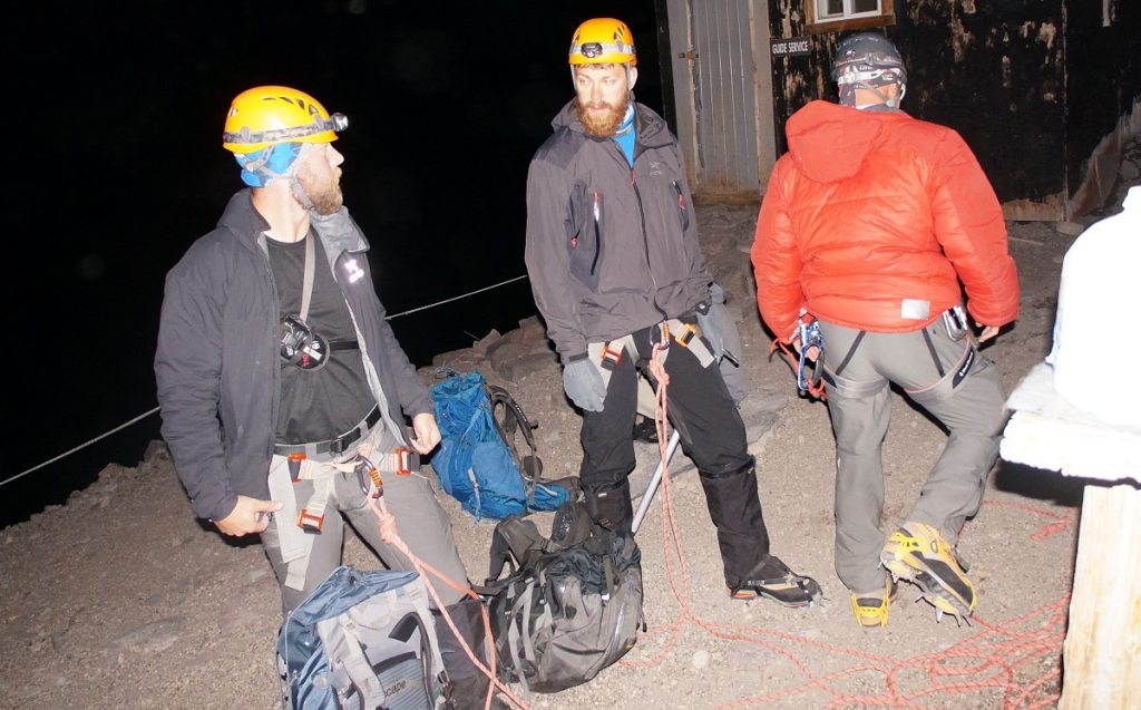 Three hikers wear gear for a midnight climb.