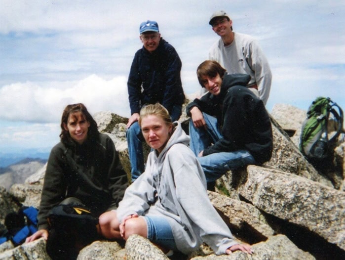 Five people sit atop a mountain on rocks.
