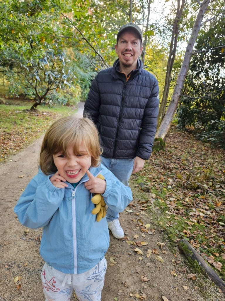 A man walks in the woods behind his 4-year-old child.
