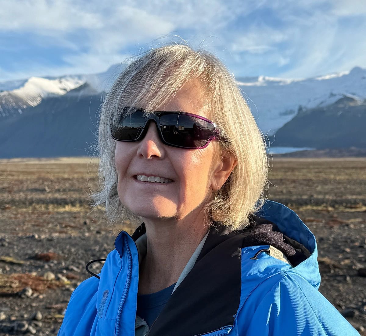 A woman with sunglasses smiles while hiking.
