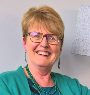 An older woman wearing glasses and a green outfit smiles for the camera.