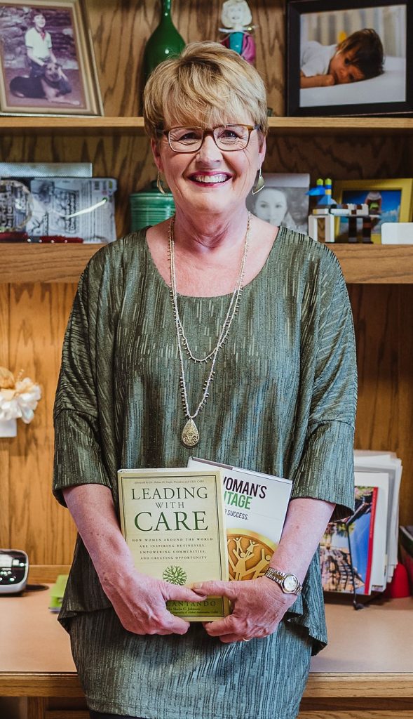 A woman stands holding two books and smiling.