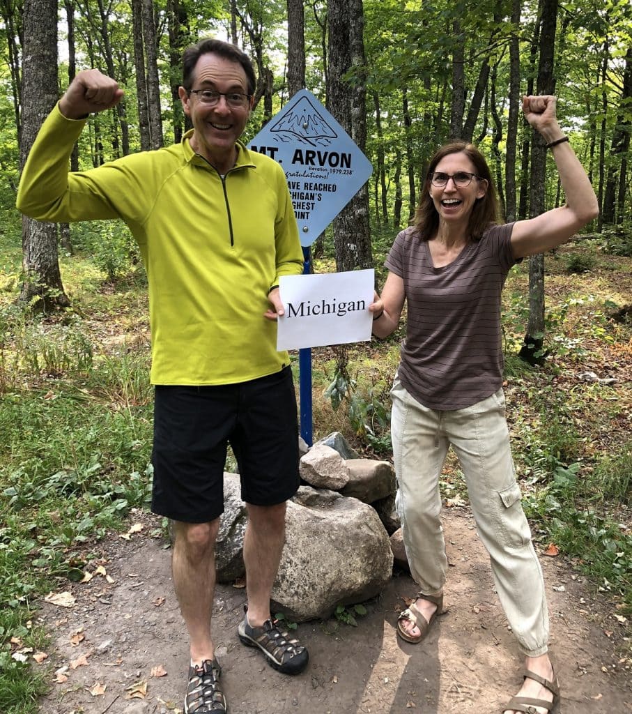 A man and woman shout with their arms up while holding a sign that says "Michigan."