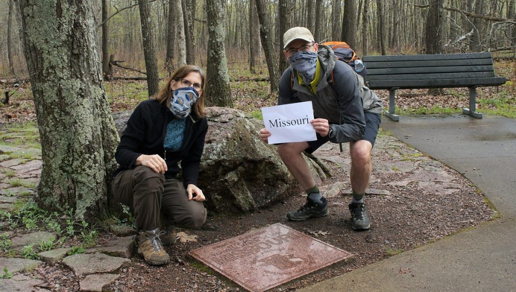 A man and woman hiker wear face masks as they hold a sign that says Missouri.
