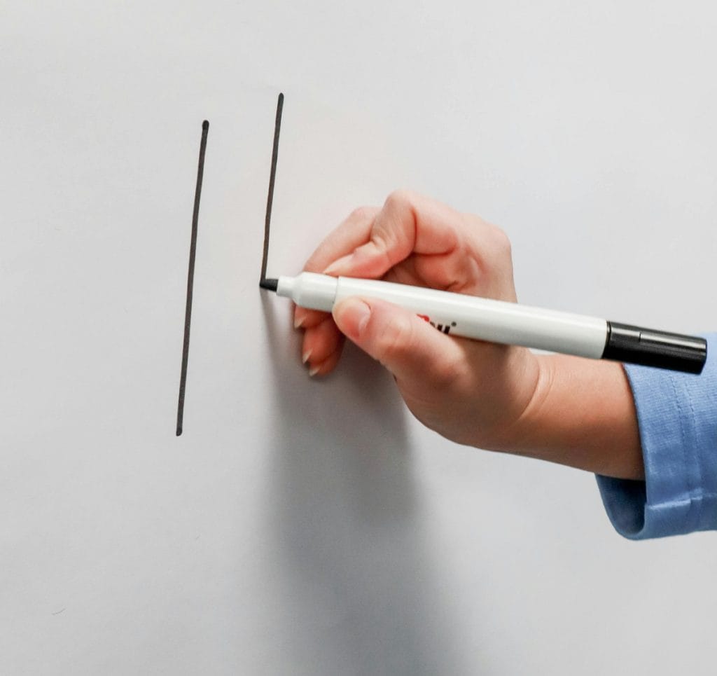 A hand holds a marker as it writes on a white board.