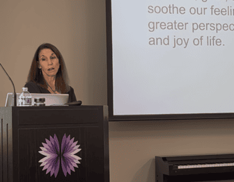 A woman stands at a podium with a power point on the screen.
