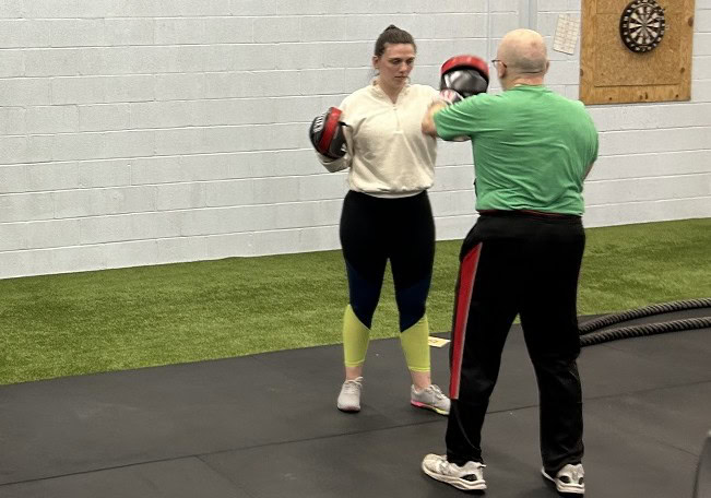 A boxing instructor practices with a student in a gym.