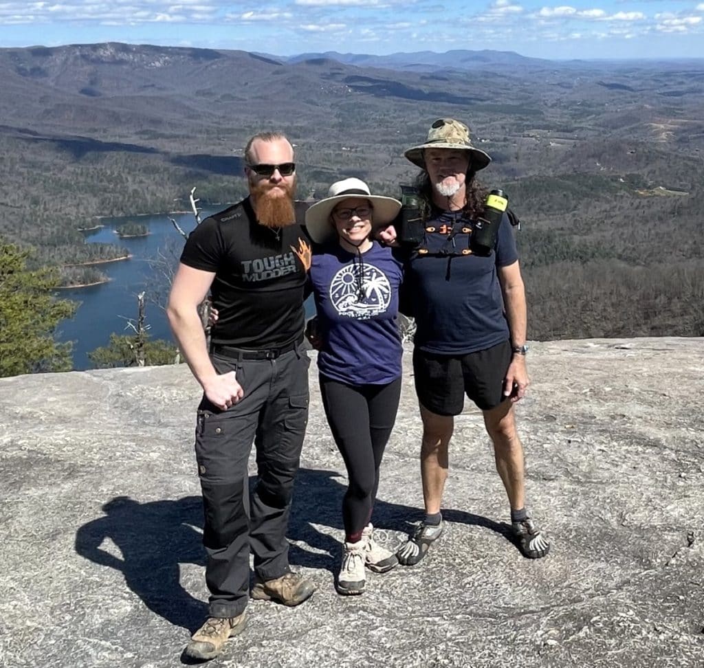 Three people are arm in arm atop a small mountain.