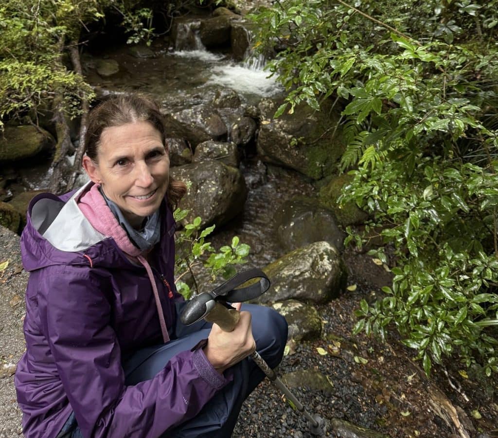 A woman sits on a rock next to a stream.