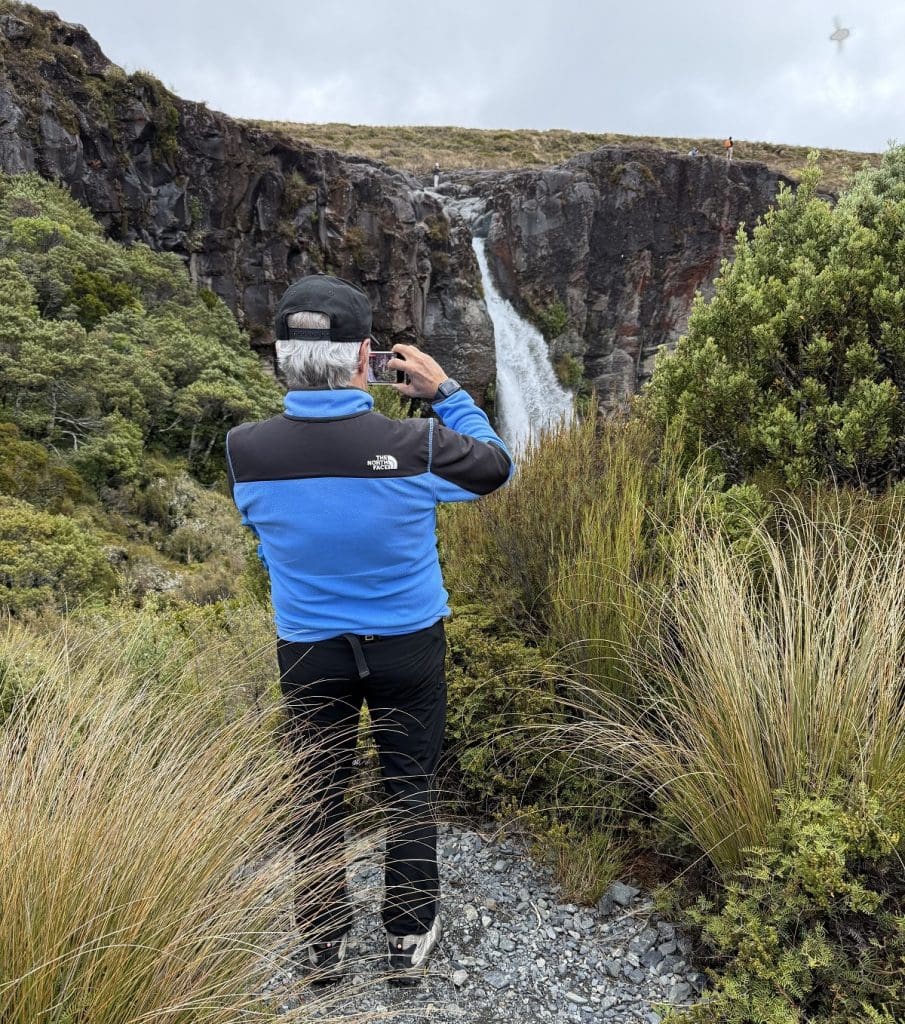 A male hiker is shown from the back taking a picture of the falls.