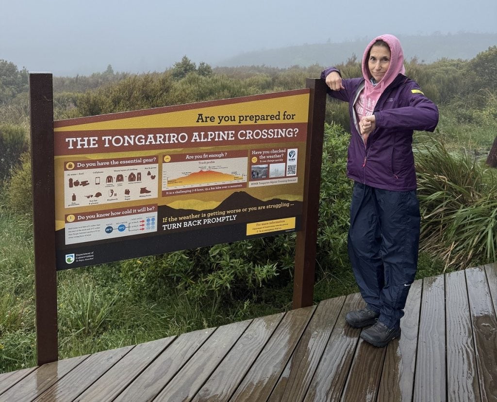 A woman stands by a sign for the trail and it's foggy in the background.