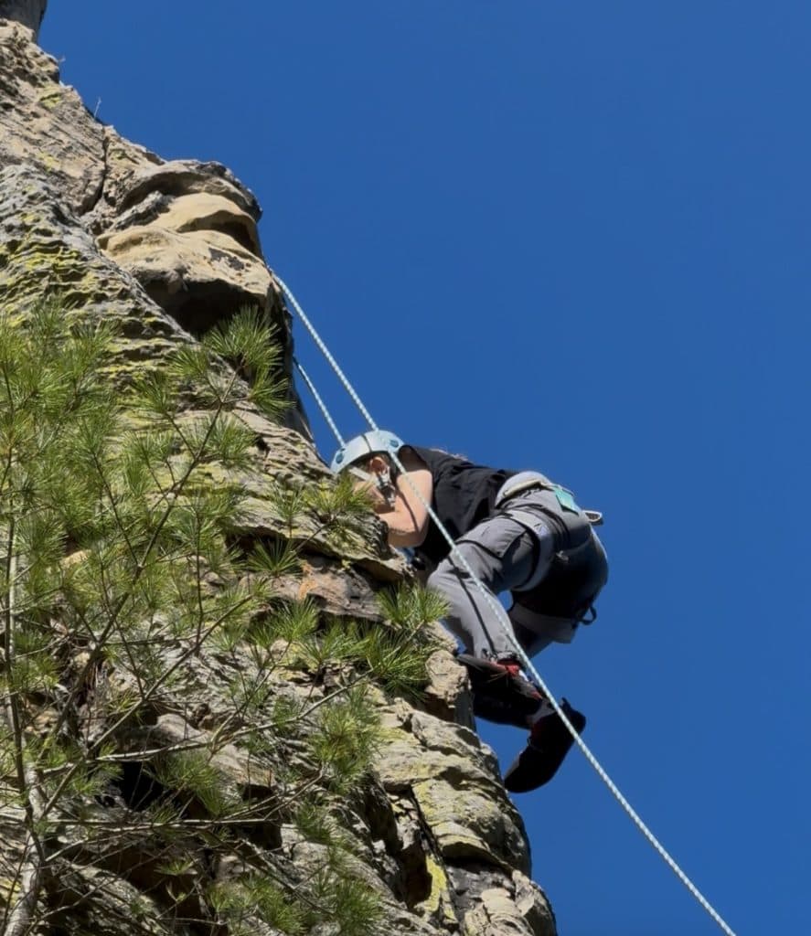 A climber hovers over a rock as the rope hangs next to her.