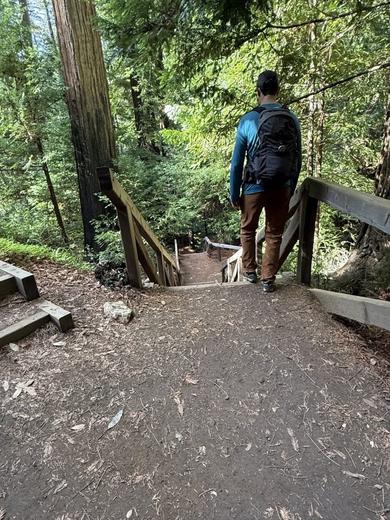 A male hiker takes a first step onto a downward staircase.