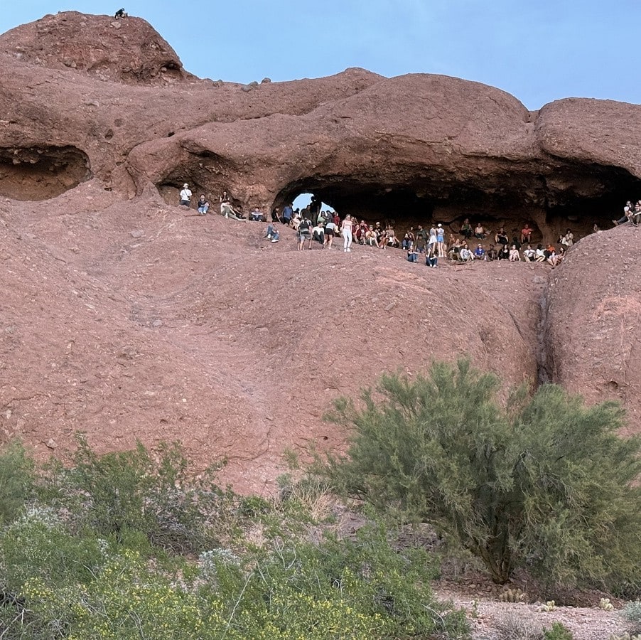 A long view of a huge butte with a front hole near the top and people gathered there.