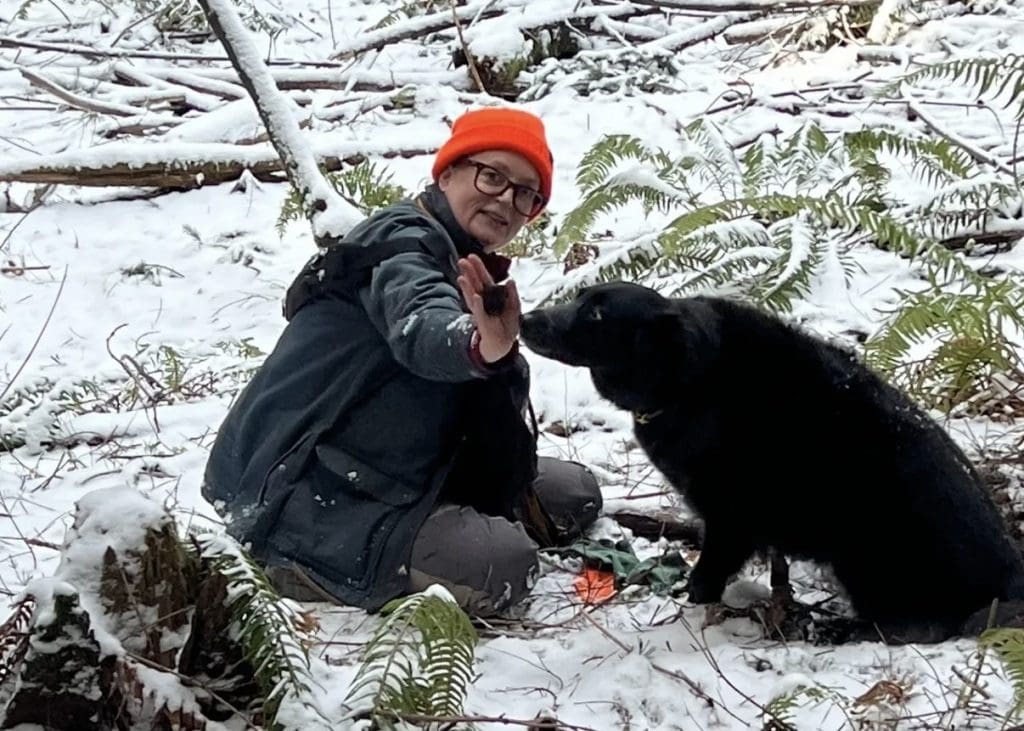 A woman and her dog sit in the woods hunting truffles.
