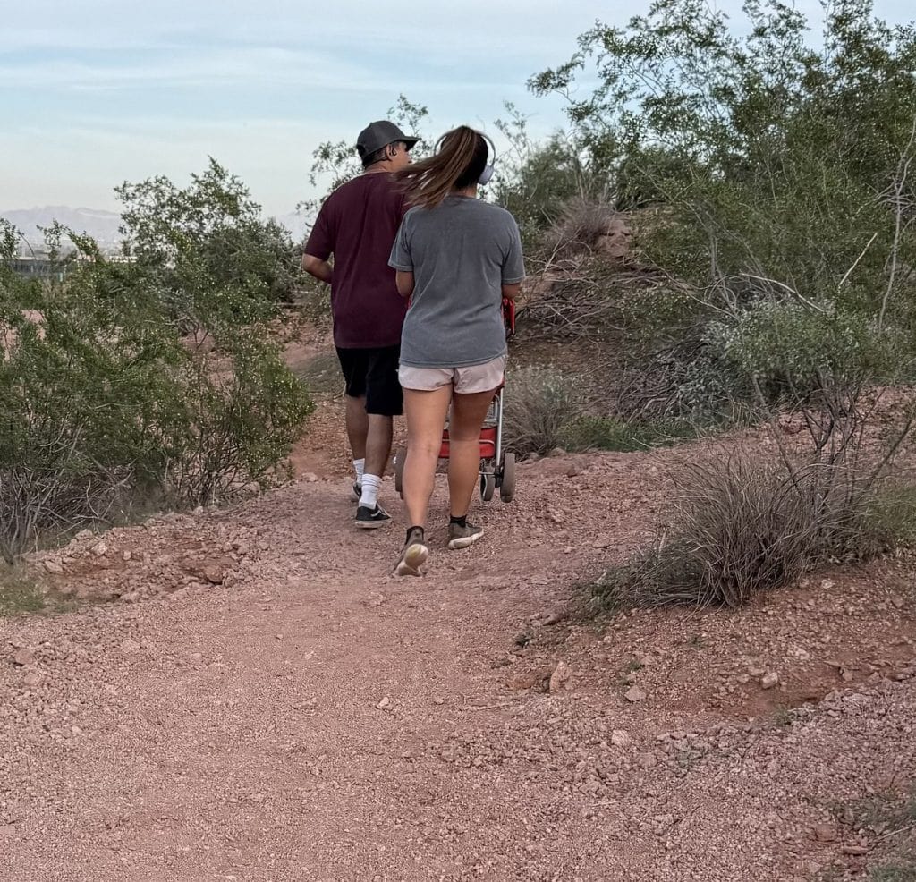 A young couple walk their dog's stroller over a dirt trail.