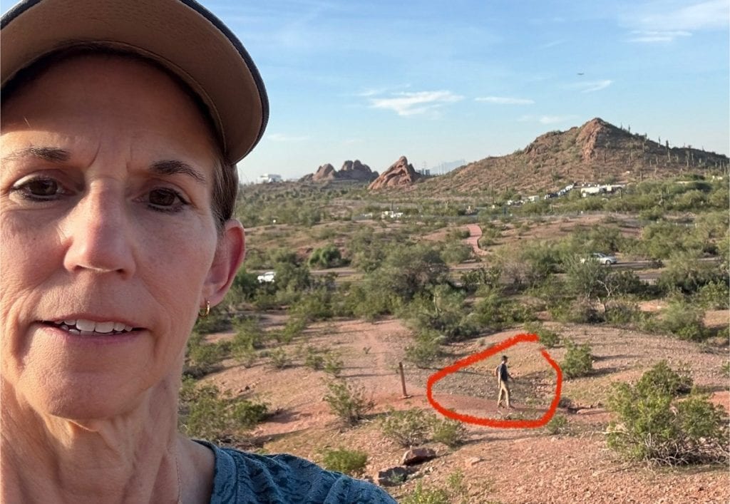 A woman in a baseball cap looks forward and a man hikes on another trail.