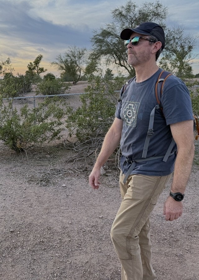 A man in a T-shirt and shorts walks along a fence.