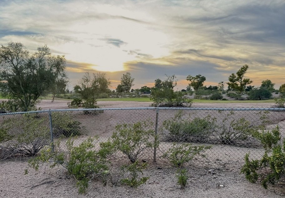 A sunset begins with a fenced golf course in the foreground.