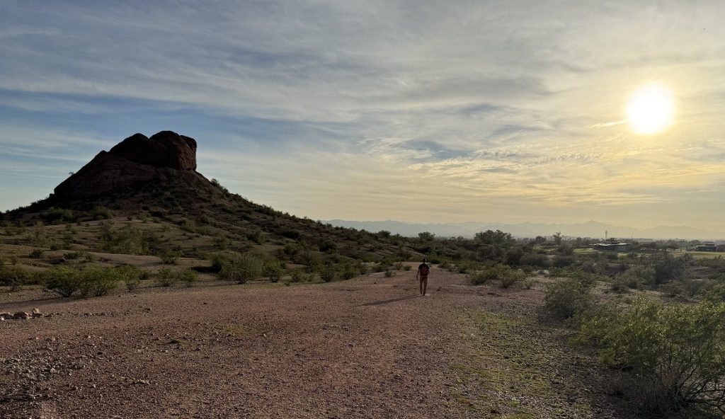 A man hikes along a crushed rock trail amid twilight.