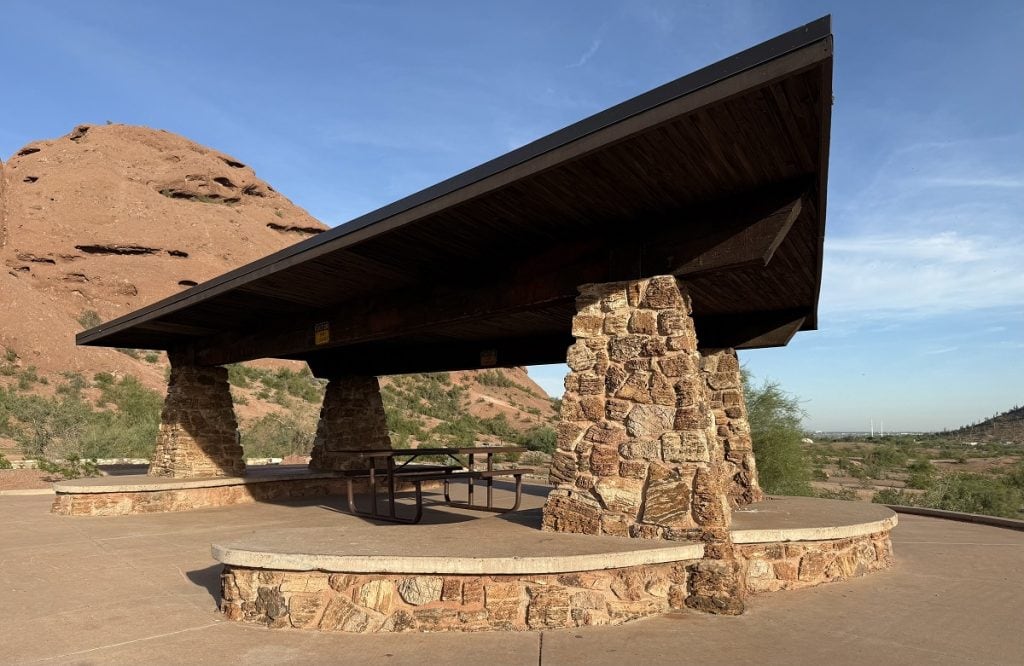 A picnic shelter with a roof is shown in the desert.