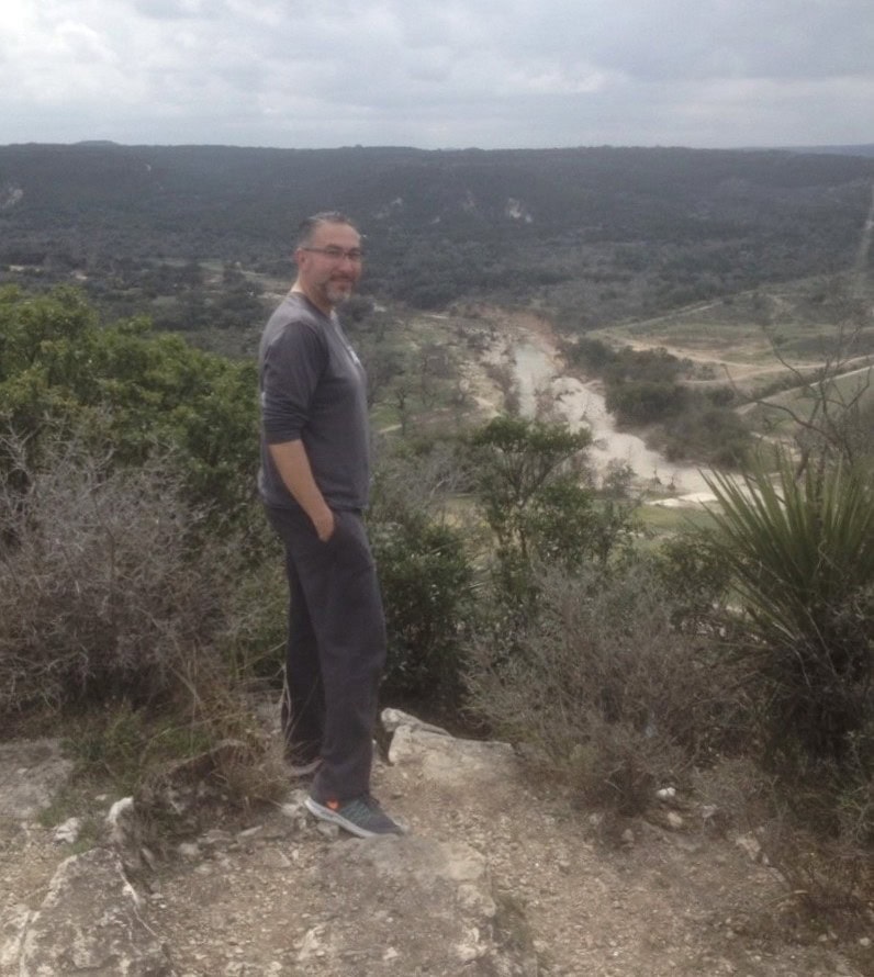 A man stands outside on a trail.