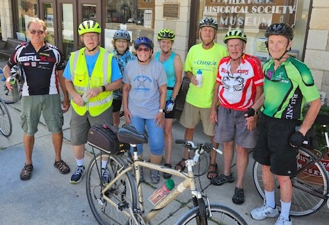 A group of several older men stand near their bicycles.