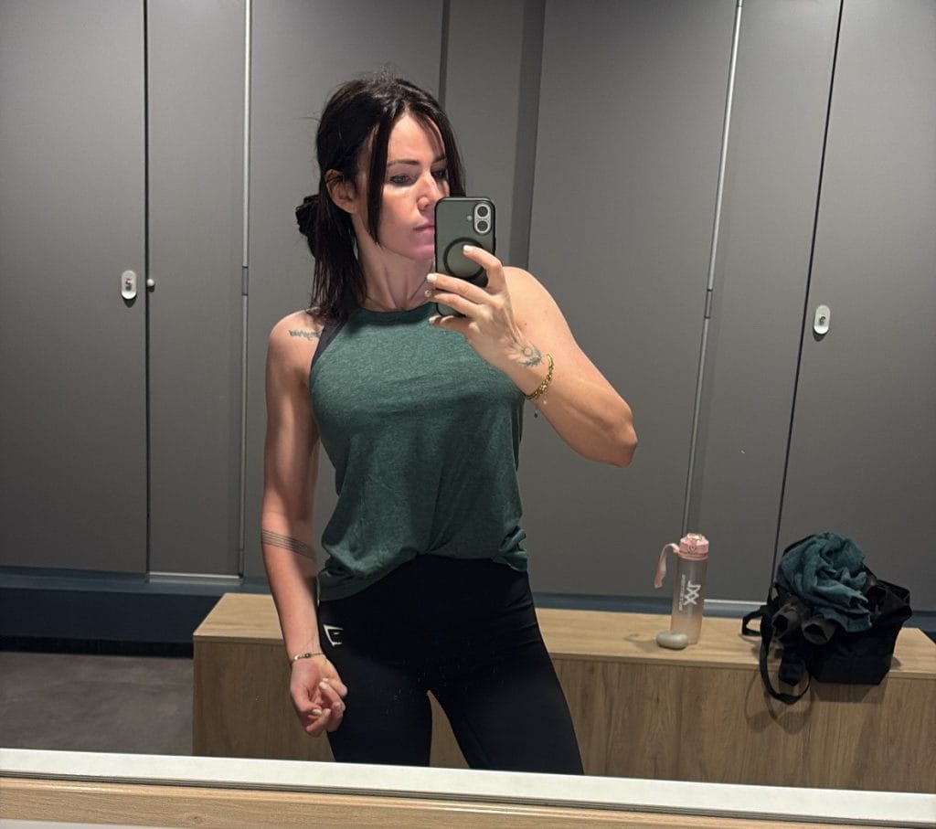 A young woman takes a selfie in a mirror in a locker room.