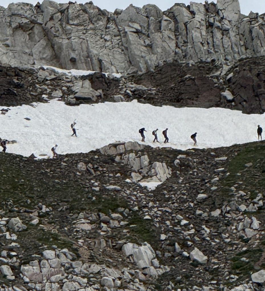 Tiny hikers are seen from far away on a snow field.
