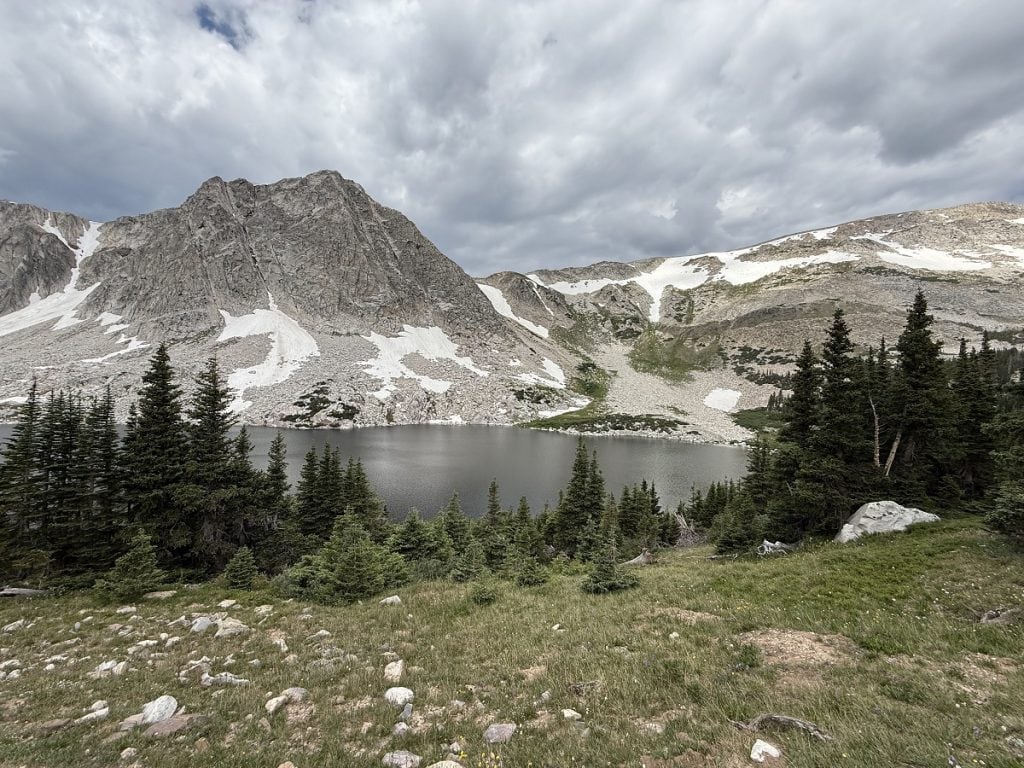 A scenic shot of mountains and pine trees and a gray colored lake.